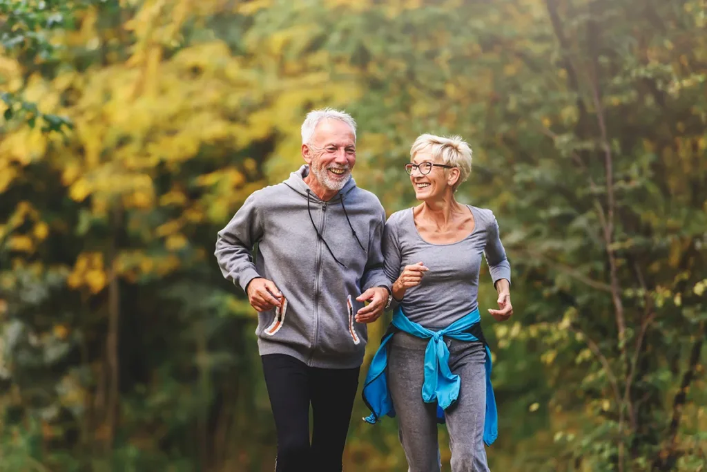 Smiling senior couple jogging in the park, symbolizing the importance of prioritizing your overall wellness to ensure optimal hearing health